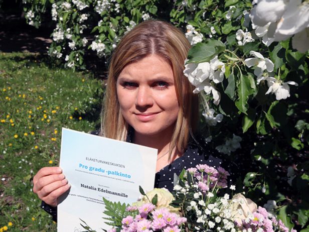 Pro gradu -palkinnon voittanut Natalia Edelmann pitää kunniakirjaa kädessään puutarhassa.