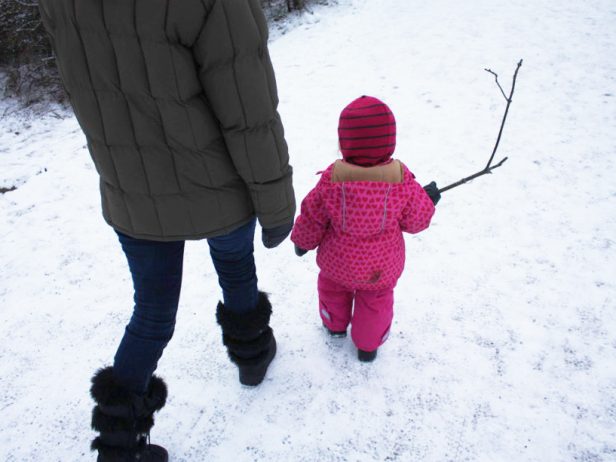 Äiti ja lapsi kävelevät lumisella tiellä.