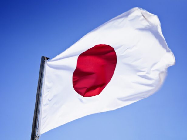 Japanin lippu liehuu sinistä taustaa vasten.